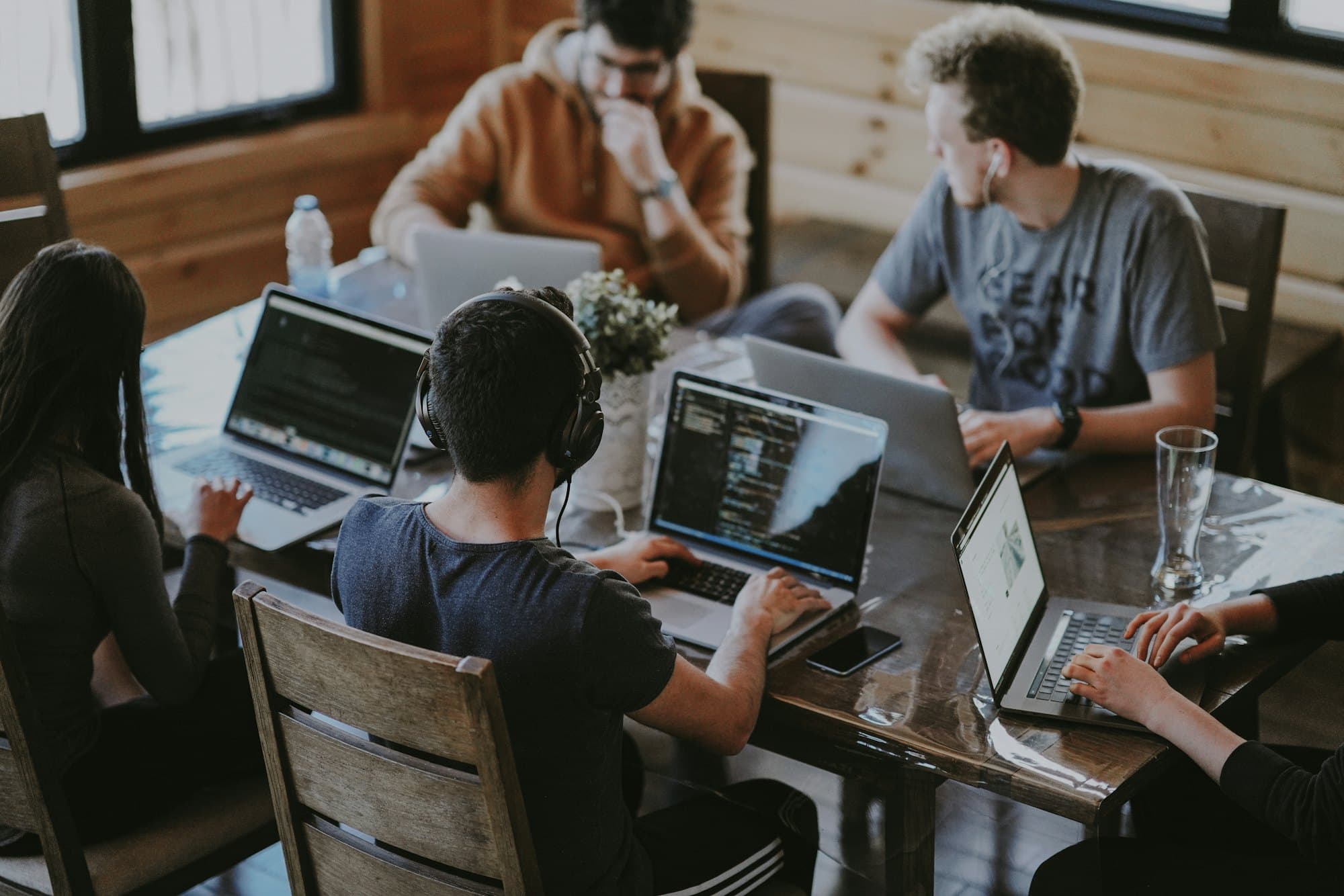 Five people working together on laptops around a long wooden table